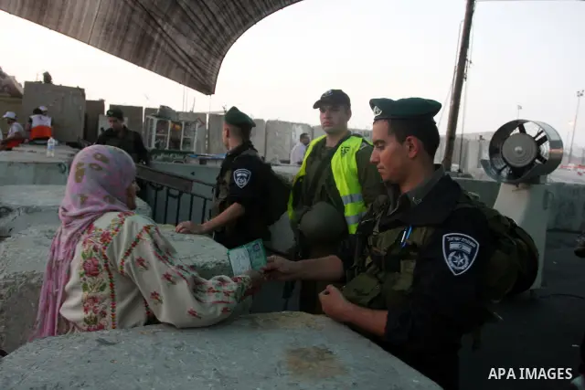 An Israeli border police officer checks documents of Palestinian women who wait to cross the Qalandia checkpoint on the outskirts of the West Bank city of Ramallah on July 20, 2012 as they head to the Al-Aqsa mosque comp...