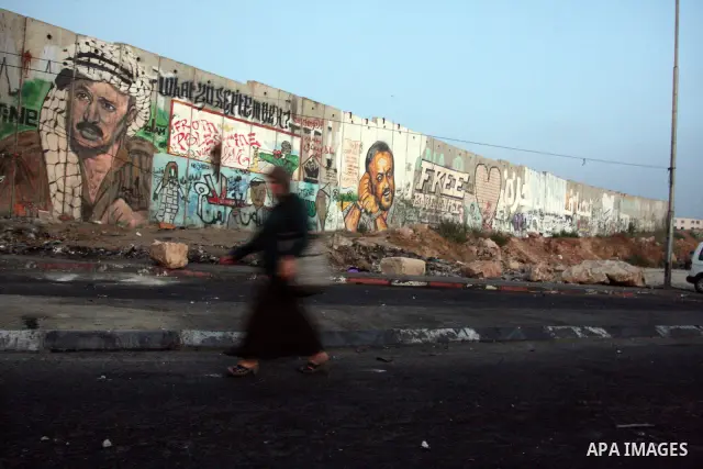 Palestinian muslim worshippers walk past a graffiti painted section of the separation wall at the Qalandia checkpoint on the outskirts of the West Bank city of Ramallah on July 20, 2012 as they head to the Al-Aqsa mosque...