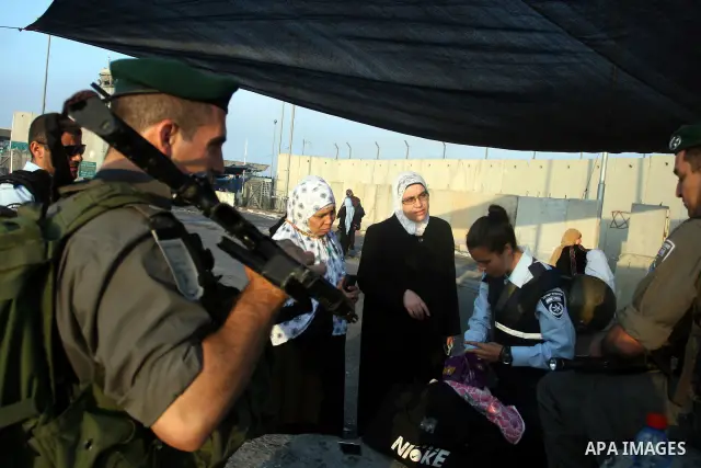 An Israeli border police officer checks documents of Palestinian women who wait to cross the Qalandia checkpoint on the outskirts of the West Bank city of Ramallah on July 20, 2012 as they head to the Al-Aqsa mosque comp...