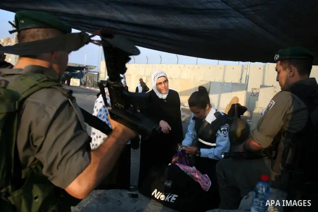 An Israeli border police officer checks documents of Palestinian women who wait to cross the Qalandia checkpoint on the outskirts of the West Bank city of Ramallah on July 20, 2012 as they head to the Al-Aqsa mosque comp...