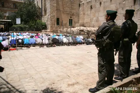 Israeli border policemen stand guard as Palestinian men perform the second Friday prayers of the Muslim fasting month of Ramadan outside the Ibrahimi Mosque or the Tomb of the Patriarchs in the West Bank city of Hebron o...