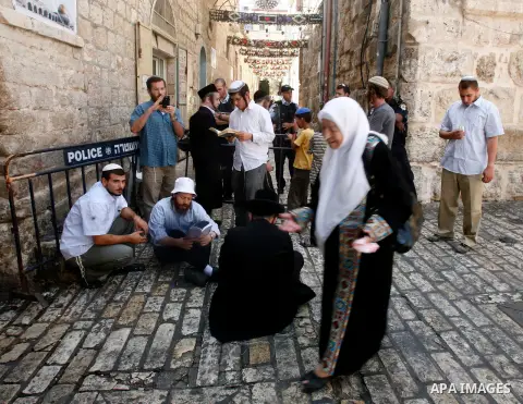 A Palestinian woman walk in front of Jewish settlers guard by Israeli policemen as they stop her walk pass of Bab Hutta road, in Jerusalem old city, on 29 July 2012. Photo by Mahfouz Abu Turk