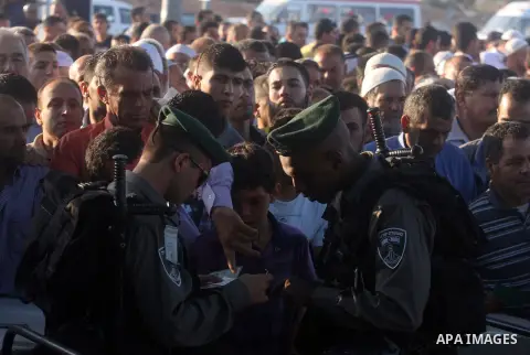 Palestinian men show their ID cards to an Israeli border policeman as they wait to cross through an military checkpoint on their way to pray at the al-Aqsa Mosque in Jerusalem, on the third Friday of the Muslim holy mont...