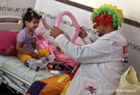 A Palestinian doctor dressed as clown, plays with a child during a physiological treatment session at a hospital in the West Bank city of Nablus, on Aug. 09, 2012. Photo by Nedal Eshtayah