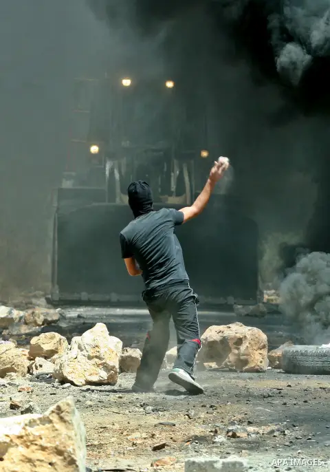 A Palestinian protester throws stones at Israeli bulldozer during a demonstration against the expropriation of Palestinian land by Israel in the village of Kafr Qaddum, near the West Bank city of Nablus, on August 10, 20...