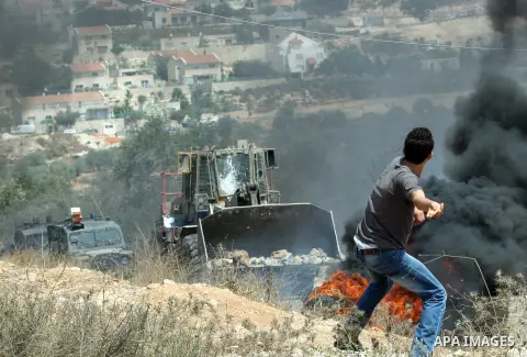 A Palestinian protestor throws stones at Israeli bulldozer during a demonstration against the expropriation of Palestinian land by Israel in the village of Kfar Qaddum, near the West Bank city of Nablus, on August 17, 20...