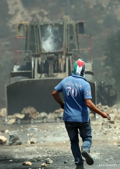 A Palestinian protestor throws stones at Israeli bulldozer during a demonstration against the expropriation of Palestinian land by Israel in the village of Kfar Qaddum, near the West Bank city of Nablus, on August 17, 20...