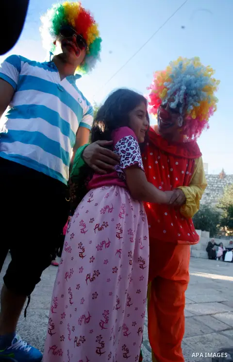 Palestinian girl plays with clowns in front of the Dome of the Rock mosque during the Eid al-Fitr prayers at al-Aqsa mosque in Jerusalem's Old City, Sunday, Aug. 19, 2012. Muslims are celebrating the festival of Eid al-F...