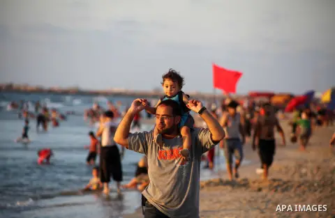 A Palestinian man carries his child at Gaza beach during Friday holiday in Gaza city, Aug 24, 2012. Gazans escape to the beach and out from their homes during heat wave and power outages. Photo by Ashraf Amra