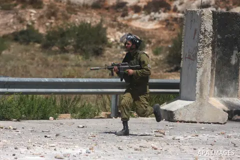 An Israeli soldier runs behind Palestinian protesters outside the Ofer military prison, near the West Bank city of Ramallah, on August 28, 2012, during a demonstration in solidarity with Palestinian prisoners being held...