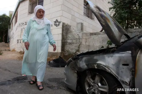 A Palestinian woman inspects a torched car and Hebrew graffiti, that reads "Death to Arabs" and "Migron", referring to the Jewish settlement of Migron, spray painted on the facade of a house by vandals believed to be Jew...