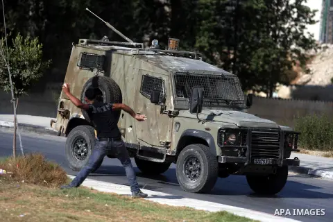 A Palestinian youth throws stones at Israeli troops vehicles as they enter Om al-Sharayet neighborhood, in the West Bank city of Ramallah, Wednesday, Aug 29, 2012. Israeli soldiers raided a store in Om al-Sharayet and le...