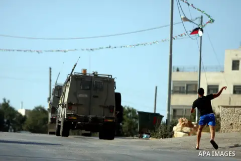 A Palestinian youth throws stones at Israeli troops vehicles as they enter Om al-Sharayet neighborhood, in the West Bank city of Ramallah, Wednesday, Aug 29, 2012. Israeli soldiers raided a store in Om al-Sharayet and le...