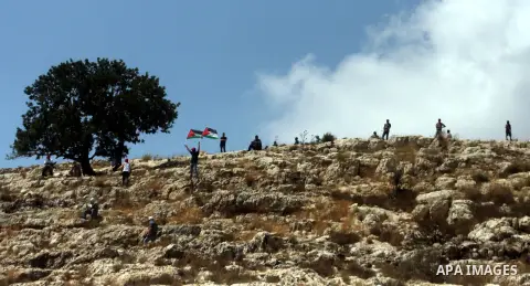 Palestinian protester waves a flag as smoke from tear gas canisters fired by Israeli security forces rises during clashes at a protest against a nearby Jewish settlement, in the West Bank village of Nabi Saleh, near Rama...