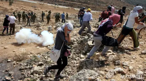 Palestinian protester waves a flag as smoke from tear gas canisters fired by Israeli security forces rises during clashes at a protest against a nearby Jewish settlement, in the West Bank village of Nabi Saleh, near Rama...