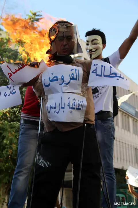 A masked Palestinian demonstrator burns an effigy of Palestinian Prime Minister Salam Fayyad during a protest against economic inequality, in the West Bank city Hebron, Tuesday, Sept 4, 2012. The death of a young Gaza ma...