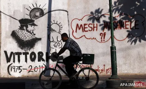 A Palestinian man ride his bicycle in front of a wall with graffiti depicting late pro-Palestinian Italian activist Vittorio Arrigoni in Gaza city, Monday, Sept. 17, 2012. A Hamas court convicted four men Monday in the a...