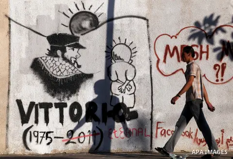 A Palestinian man walks in front of a wall with graffiti depicting late pro-Palestinian Italian activist Vittorio Arrigoni in Gaza city, Monday, Sept. 17, 2012. A Hamas court convicted four men Monday in the abduction an...
