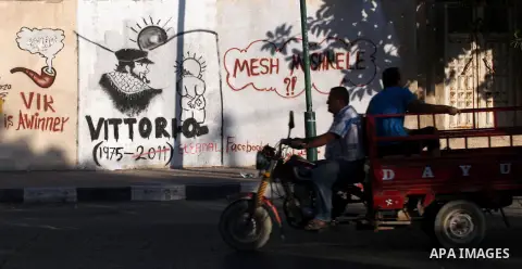 Palestinians ride a motorcycle in front of a wall with graffiti depicting late pro-Palestinian Italian activist Vittorio Arrigoni in Gaza city, Monday, Sept. 17, 2012. A Hamas court convicted four men Monday in the abduc...