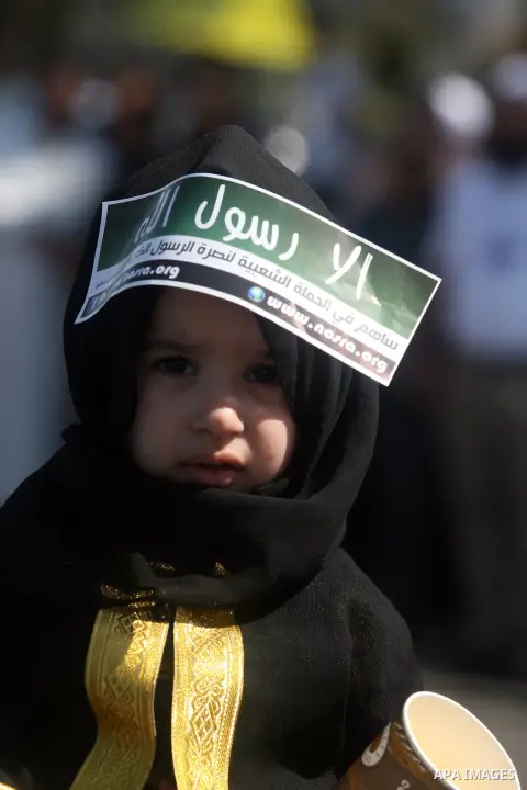 A Palestinian girl holds a banner reading in Arabic "Anyone but prophet Muhammad" and shout slogans during a protest in the West Bank town of Ramallah against an anti-Islam movie made in the U.S. and French cartoons said...