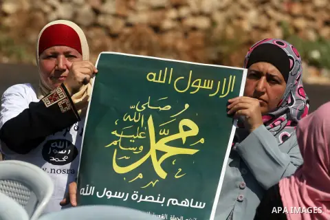 Palestinian woman hold a banner reading in Arabic "Anyone but prophet Muhammad" and shout slogans during a protest in the West Bank town of Ramallah against an anti-Islam movie made in the U.S. and French cartoons said t...