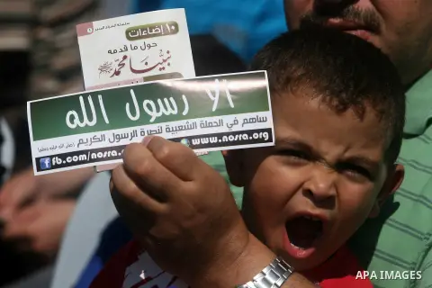 A Palestinian man with his son hold a banner reading in Arabic "Anyone but prophet Muhammad" and shout slogans during a protest in the West Bank town of Ramallah against an anti-Islam movie made in the U.S. and French ca...