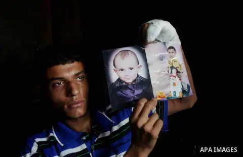 A Palestinian father hold picture a photograph of one-year-old Fathi Baghdadi, who died after a fire from a candle that swept through their home in the Bureij refugee camp in the center of the Gaza Strip on September 26,...