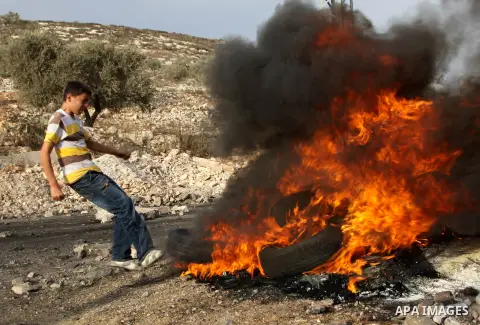 A Palestinian protester burns tires after a demonstration against the expropriation of Palestinian land by Israel in the village of Kfar Qaddum, near the West Bank city of Nablus,Palestinian protesters throw stones at Is...