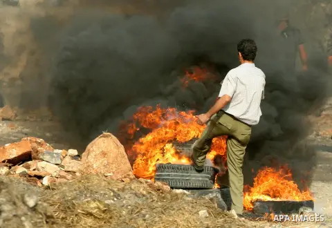 A Palestinian protester burns tires after a demonstration against the expropriation of Palestinian land by Israel in the village of Kfar Qaddum, near the West Bank city of Nablus,Palestinian protesters throw stones at Is...