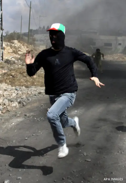 A masked Palestinian protester runs near an Israeli soldier during clashes following a demonstration against the expropriation of Palestinian land by Israel in the village of Kafr Qadum in the occupied West Bank on Octob...