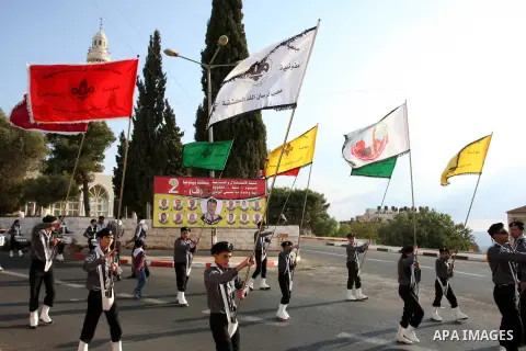 Palestinian Youth holds national flags as he walks past an electoral poster displaying portraits of candidates running for municipal elections on October 6, 2012 in the West Bank city of Ramallah. Campaigning has started...