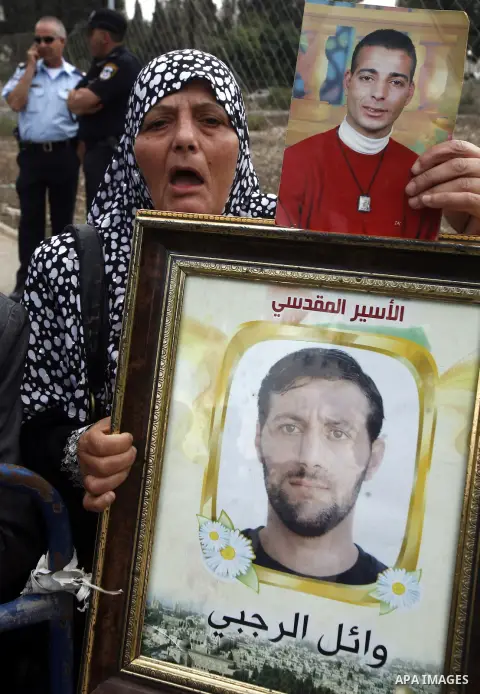 Families of Palestinian prisoners in Israeli jails hold their portraits and placards, bearing a portrait of Israeli soldier Gilad Shalit on the emblem of Spanish FC Barcelona football club, during a demonstration outside...