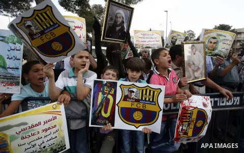Families of Palestinian prisoners in Israeli jails hold their portraits and placards, bearing a portrait of Israeli soldier Gilad Shalit on the emblem of Spanish FC Barcelona football club, during a demonstration outside...