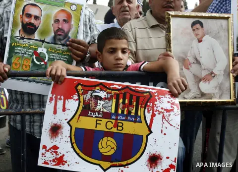 Families of Palestinian prisoners in Israeli jails hold their portraits and placards, bearing a portrait of Israeli soldier Gilad Shalit on the emblem of Spanish FC Barcelona football club, during a demonstration outside...