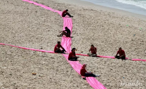 Palestinian youths sit on a beach in Gaza City near a pink ribbon as part of the Breast Cancer Awareness campaign on October 10, 2012. Photo by Majdi Fathi