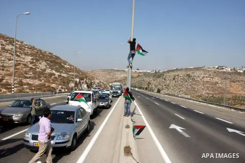 A Palestinian activist places a flag on a pole as others block part of the 443 highway during a protest near the West Bank village of Beit Ur against what they say are attacks by Jewish settlers on Palestinians and their...