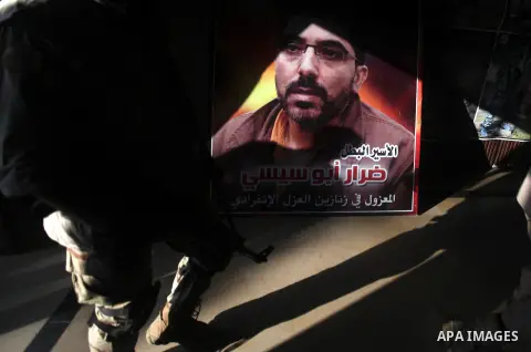 A Palestinian Hamas militant walks pass next to a portrait of a Palestinian prisoner during a ceremony to mark the first anniversary of a deal which saw the exchange of 1,027 Palestinian prisoners for captured Israeli so...