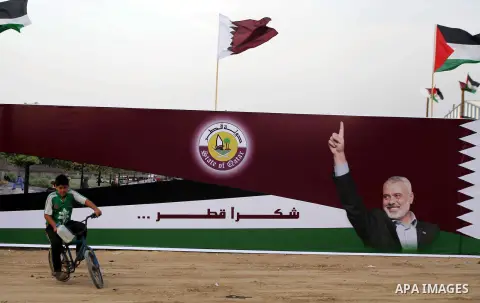 A Palestinian child rides his bicycle in front of the image of Palestinian Prime Minister in Gaza strip Ismail Haniyeh, adorn's a barrier where a project funded by Qatar is under construction, in Gaza City on October 21,...