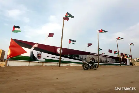 A Palestinian man rides his motorcycle in front of the image of the Emir of Qatar, Sheikh Hamad bin Khalifa Al-Thani, adorn's a barrier where a project funded by Qatar is under construction, in Gaza City on October 21, 2...