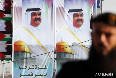 A Palestinian Hamas security officer stands guard on Gaza's main road as he and others wait for the convoy of the Qatari Emir Sheikh Hamad bin Khalifa Al-Thani, depicted in banners behind, to arrive in Gaza City, Tuesday...