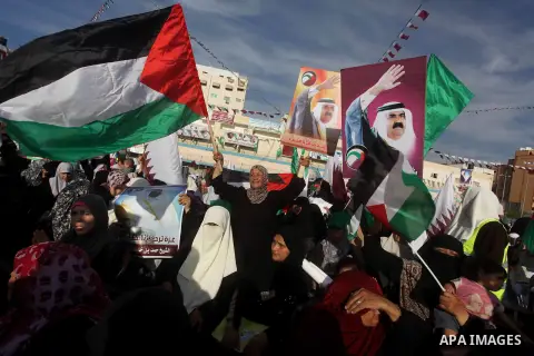 Palestinian Hamas supporters wave Qatari and Palestinian flags as others hold posters of the Emir of Qatar Sheikh Hamad bin Khalifa al-Thani, not pictured, as they wait for him to give a speech at the Palestine stadium i...