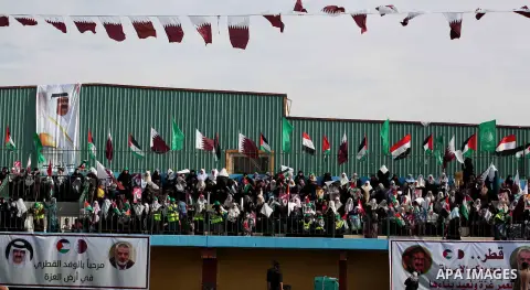 Palestinian Hamas supporters wave Qatari and Palestinian flags as others hold posters of the Emir of Qatar Sheikh Hamad bin Khalifa al-Thani, not pictured, as they wait for him to give a speech at the Palestine stadium i...