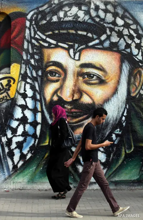 Palestinians passe by a mural depicting late Palestinian leader Yasser Arafat in Gaza City on Oct. 31, 2012. Palestinian authorities confirmed the November timetable to exhume the remains of former Palestinian leader Yas...