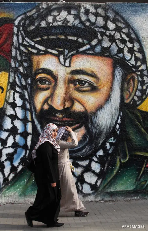 Palestinians passe by a mural depicting late Palestinian leader Yasser Arafat in Gaza City on Oct. 31, 2012. Palestinian authorities confirmed the November timetable to exhume the remains of former Palestinian leader Yas...