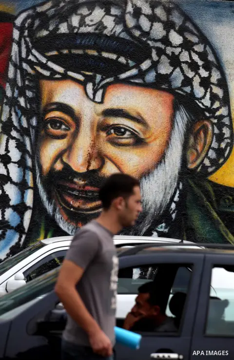 Palestinians passe by a mural depicting late Palestinian leader Yasser Arafat in Gaza City on Oct. 31, 2012. Palestinian authorities confirmed the November timetable to exhume the remains of former Palestinian leader Yas...