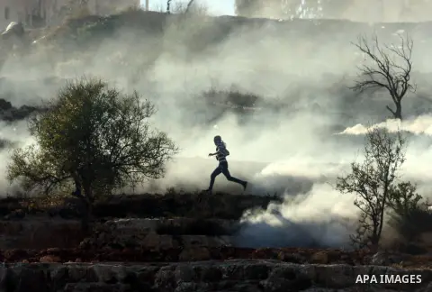 A Palestinian demonstrator runs through a cloud of tear gas during clashes against Israel's operations in Gaza Strip, outside Ofer, an Israeli military prison near the West Bank city of Ramallah, Thursday, Nov. 15, 2012....