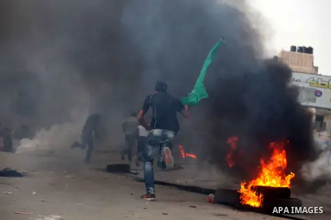 A Palestinian stone-thrower walks past smoke from burning tyres during clashes with Israeli security forces against Israel's military operation in Gaza, at Qalandia checkpoint near the West Bank city of Ramallah November...