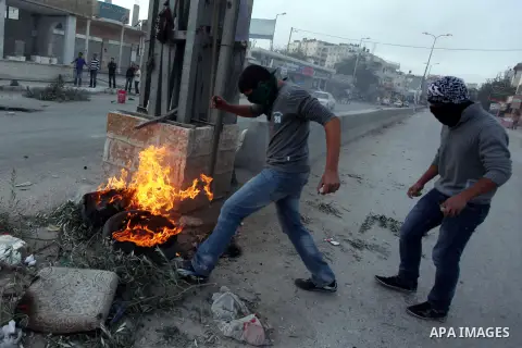 A Palestinian stone-thrower walks past smoke from burning tyres during clashes with Israeli security forces against Israel's military operation in Gaza, at Qalandia checkpoint near the West Bank city of Ramallah November...