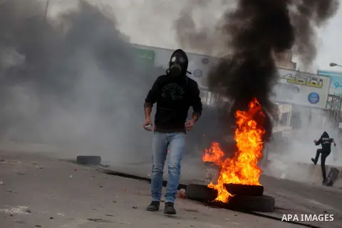A Palestinian stone-thrower walks past smoke from burning tyres during clashes with Israeli security forces against Israel's military operation in Gaza, at Qalandia checkpoint near the West Bank city of Ramallah November...