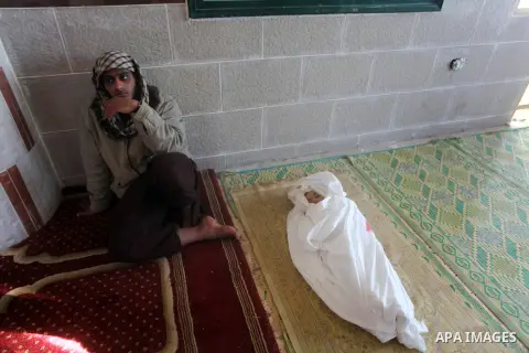 A Palestinian man sits next to the body of his year-and-a-half old son Iyad Abu Khoussa, during his funeral in Bureij Refugee Camp, central Gaza Strip, Sunday, Nov. 18, 2012. The baby boy was one of five Palestinian chil...